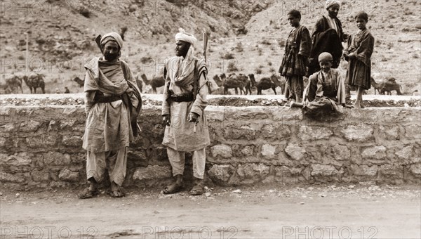 Armed frontier guards. Two armed guards, identified as 'Frontier Constabulary' officers, stand against a stone wall with their rifles slung over their shoulders. Their lack of uniform suggests they may be 'Khassadars', members of a locally administered force who were given government allowances in return for protecting the frontier. North West Frontier Province, India (Pakistan), circa 1927., North West Frontier Province, Pakistan, Southern Asia, Asia.