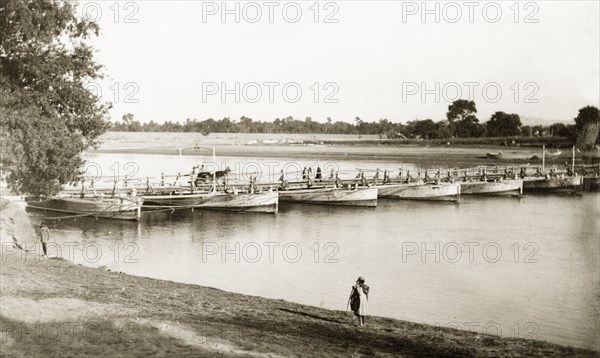Boats used as pontoons for a bridge, India. A number of boats are used as pontoons to support a small footbridge over the Kabul River. Nowshera, North West Frontier Province, India (Pakistan), circa 1925. Nowshera, North West Frontier Province, Pakistan, Southern Asia, Asia.