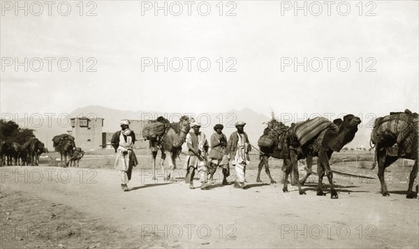 Driving camels along the Khyber Pass. Indian men drive camels laden with bundles of supplies past a fort on the Khyber Pass, a strategically important route in the Safed Koh Mountains, connecting British India (now Pakistan) with Afghanistan. North West Frontier Province, India (Pakistan), circa 1924., North West Frontier Province, Pakistan, Southern Asia, Asia.