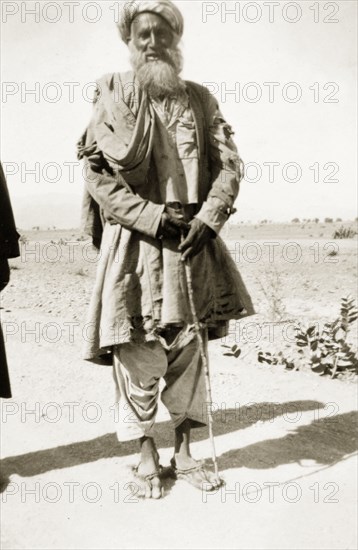 An elderly Afridi man. Full-length portrait of an elderly Afridi man, dressed in traditional costume including sandals and a turban, and holding a walking stick. North West Frontier Province, India (Pakistan), circa 1927., North West Frontier Province, Pakistan, Southern Asia, Asia.