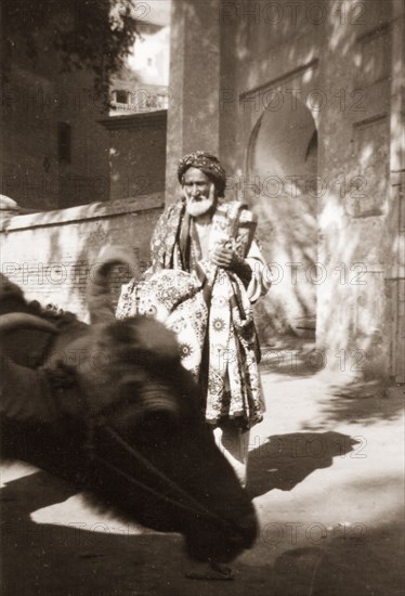 An Indian rug vendor. An elderly street trader touts a variety of patterned rugs as he wanders around the city streets looking for custom. North West Frontier Province, India (Pakistan), circa 1927., North West Frontier Province, Pakistan, Southern Asia, Asia.