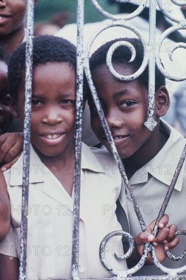 Two Jamaican schoolchildren. An official Jamaican Tourist Board photograph features two curious schoolchildren peering through iron railings at the Spanish Town Elementary School. Spanish Town, Jamaica, circa 1985. Spanish Town, St Catherine, Jamaica, Caribbean, North America .