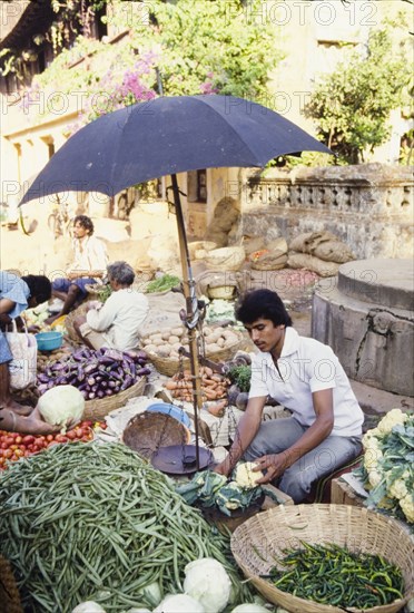 Weighing vegetables at a market in Goa. A man weighs cauliflowers on a pair of scales shaded by an umbrella, at a fruit and vegetable market in Goa. Goa, India, circa 1985., Goa, India, Southern Asia, Asia.