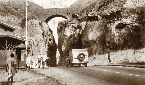 The main pass between the crater and Steamer Point'. A motorcar drives along the pass linking Steamer Point to the crater of an extinct volcano. The road passes beneath an arched bridge, through a gorge carved into the volcanic rock. Aden, Yemen, 1943. Aden, Adan, Yemen, Middle East, Asia.