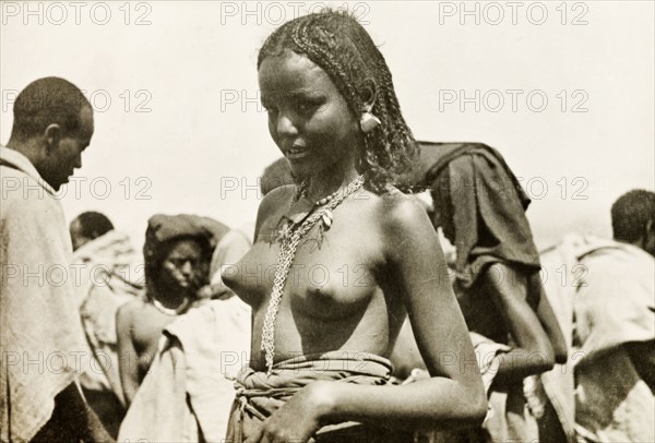 A young Eritrean woman. Portrait of a young Eritrean woman, taken at an outdoor camel market. Naked from the waist up, her hair is braided and she wears a decorative necklace and earrings. Eritrea, 1943. Eritrea, Eastern Africa, Africa.