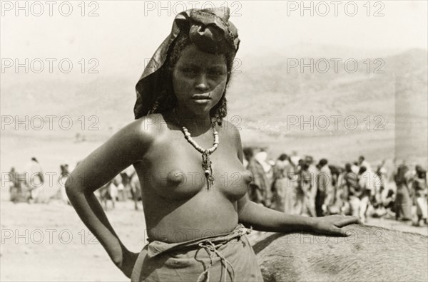 A young Eritean woman. Portrait of a young Eritean woman at a camel market. Naked from the waist up, she stands with one hand on her hip, wearing a headscarf and a beaded necklace. Eritrea, 1943. Eritrea, Eastern Africa, Africa.