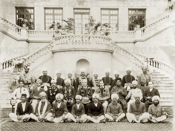 Dignitaries at Government House in Lahore. British and Indian dignitairies assemble for a group portrait at the foot of a grand staircase inside Government House. Four officials seated in the middle row wear garlands of flowers strung around their necks. Lahore, Punjab, India (Pakistan), 1919. Lahore, Punjab, Pakistan, Southern Asia, Asia.