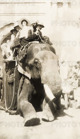 Europeans take an elephant ride, India. A group of smiling European people sit in a howdah on the back of an elephant as they prepare for a ride. The elephant's mahout (elephant handler) sits on its shoulders, 'ankusha' in hand. Lahore, Punjab, India (Pakistan), 3 April 1920. Lahore, Punjab, Pakistan, Southern Asia, Asia.