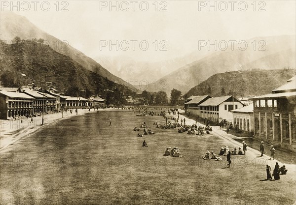 Relaxing on the grassy sward at Chaugan. People mill about and relax on the wide, grassy sward in the centre of Chaugan. The sward was established by the British as a public promenade and recreation ground to play sports such as cricket. Chaugan, Chamba, Simla Hill States (Himachal Pradesh), India, circa 25 April 1920. Chamba, Himachal Pradesh, India, Southern Asia, Asia.