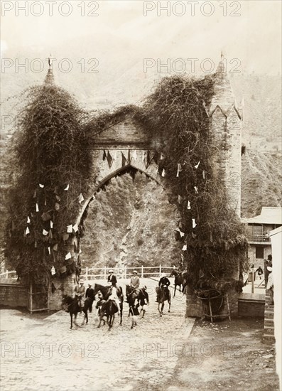 British government officers arrive in Chamba. Four British government officers, accompanied by an escort of Indian guards, ride on horseback through a decorated stone arch upon arrival in Chamba. Chamba, Simla Hill States (Himachal Pradesh), India, circa April 1920. Chamba, Himachal Pradesh, India, Southern Asia, Asia.