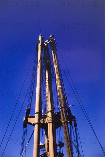 Sailor on the mast of M.V. Obuasi. A sailor stands at the top of a ladder on the stern mast of a cargo ship, M.V. Obuasi, adjusting or repairing the rigging. Ghana, circa 1960. Ghana, Western Africa, Africa.