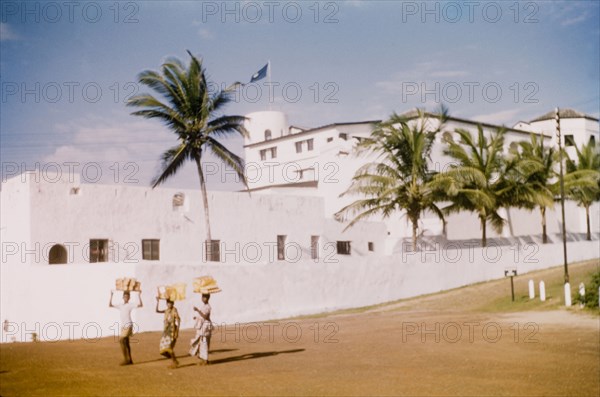 Breadsellers at Elmina Castle. Three breadsellers walk along a road adjacent to Elmina Castle. Elmina, Ghana, circa 1959. Elmina, Central (Ghana), Ghana, Western Africa, Africa.