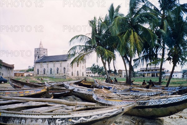 Painted fishing boats at Anomabu. A collection of painted fishing boats lie on the sand close to a colonial-style Methodist church. Anomabu, Ghana, January 1958. Anomabu, Central (Ghana), Ghana, Western Africa, Africa.