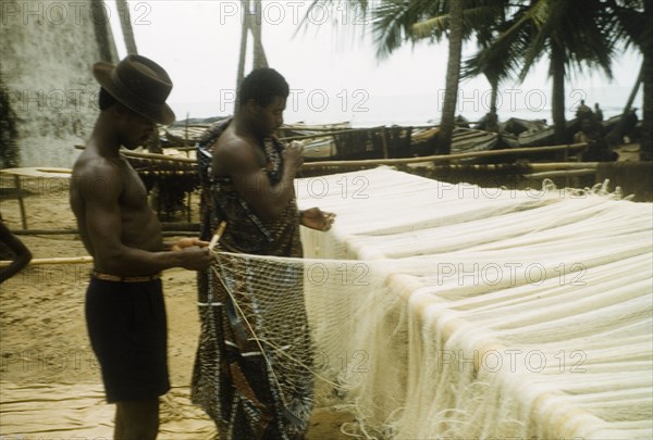 Mending the nets. Two men repair fishing nets at Anomabu beach. Anomabu, Ghana, January 1958. Anomabu, Central (Ghana), Ghana, Western Africa, Africa.