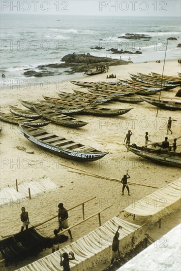 Fishing beach at Anomabu. A beach at Anomabu, covered with painted fishing boats and rows of fishing nets strung over poles. Anomabu, Ghana, January 1958. Anomabu, Central (Ghana), Ghana, Western Africa, Africa.