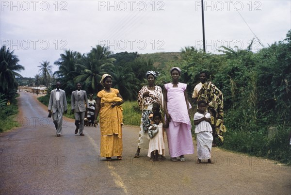 Churchgoers in Abandze. Families dressed in their Sunday best walk along a road to attend church in Abandze. Abandze, Ghana, circa 1958. Abandze, Central (Ghana), Ghana, Western Africa, Africa.