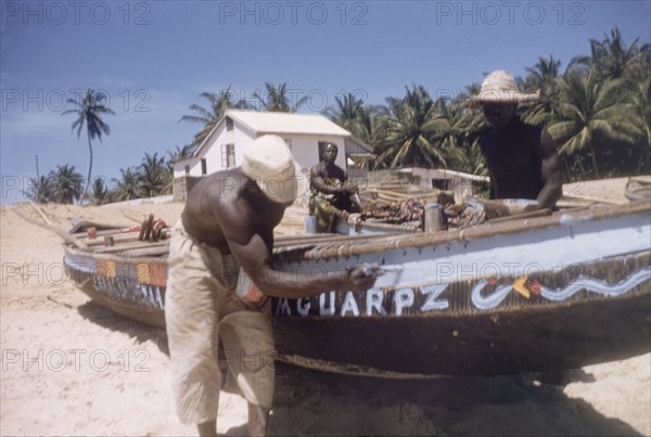 Painting canoes on Prampram beach. Men paint fishing canoes on the beach at Prampram. Near Accra, Ghana, October 1958. Accra, East (Ghana), Ghana, Western Africa, Africa.