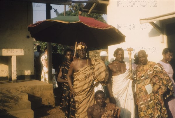 The Adontenhene of Akuapem. The Adontenhene of Akuapem, Nana Osae Djan II, stands beneath a ceremonial umbrella, surrounded by Ghanaian elders. Aburi, Ghana, circa 1960. Aburi, East (Ghana), Ghana, Western Africa, Africa.