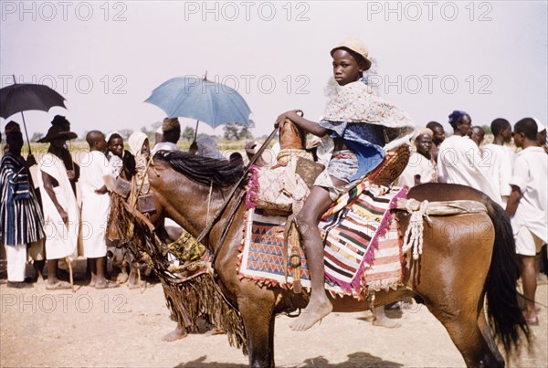 Boy riding a caparisoned pony. A boy, possibly the son of a chief, rides a caparisoned pony at anniversary during celebrations for the fourth anniversary of Ghanaian independence. Savelugu, Ghana, circa March 1961. Savelugu, North (Ghana), Ghana, Western Africa, Africa.