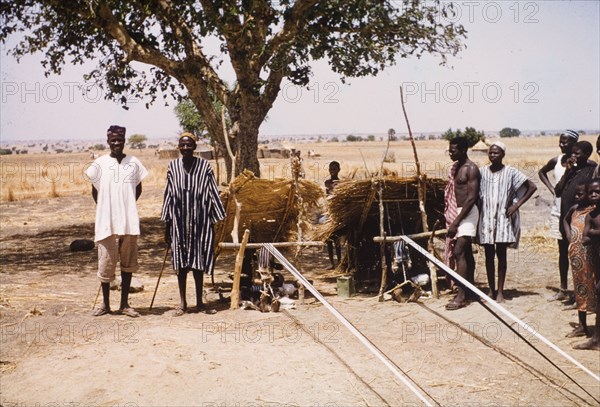 Boys weaving cloth at Pusiga, Ghana. Two young boys sit outdoors beneath thatched sun shelters as they weave strip cloth using heddle looms. Pusiga, Ghana, circa 1960. Pusiga, Upper East, Ghana, Western Africa, Africa.