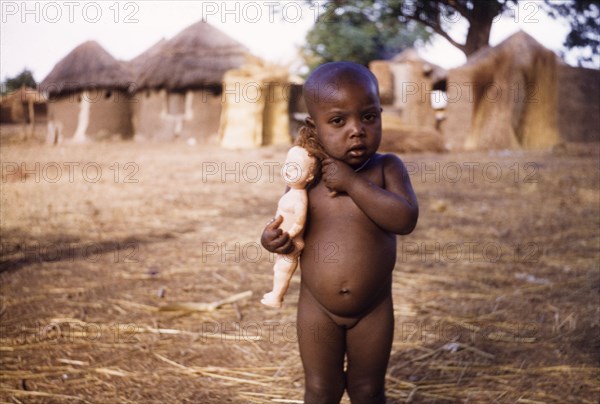 Ghanaian toddler with a European-style doll. Portrait of a naked young girl, aged about three, clutching a European-style doll. Near Bawku, Ghana, circa 1960. Bawku, Upper East, Ghana, Western Africa, Africa.