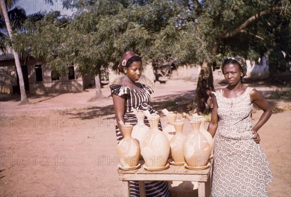 Water cooler sellers at Koloenu. Two female water cooler sellers stand at their roadside stall. Koloenu, Ghana, circa 1960. Koloenu, Volta, Ghana, Western Africa, Africa.