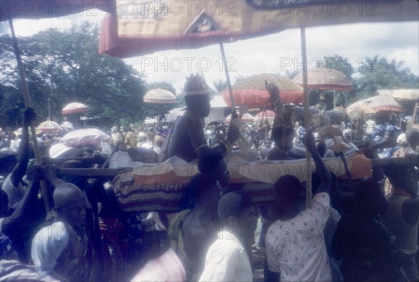 Mate Kole II at a Ngmayem festival. Mate Kole II (1910-1990), the Paramount Chief or Konor of Manya Krobo, is ferried along in a palanquin during an annual Ngmayem harvest festival procession. He wears a ceremonial headdress and holds a staff in one hand. Odumasi, Ghana, circa 1960. Odumasi, East (Ghana), Ghana, Western Africa, Africa.