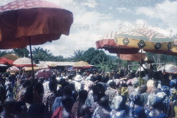 Crowds at a Ngmayem festival. Crowds of people celebrate an annual Ngmayem harvest festival at Odumasi. Several Manya Krobo chiefs carry staffs as they are ferried along in palanquins shaded by umbrellas. Odumasi, Ghana, circa 1960. Odumasi, East (Ghana), Ghana, Western Africa, Africa.
