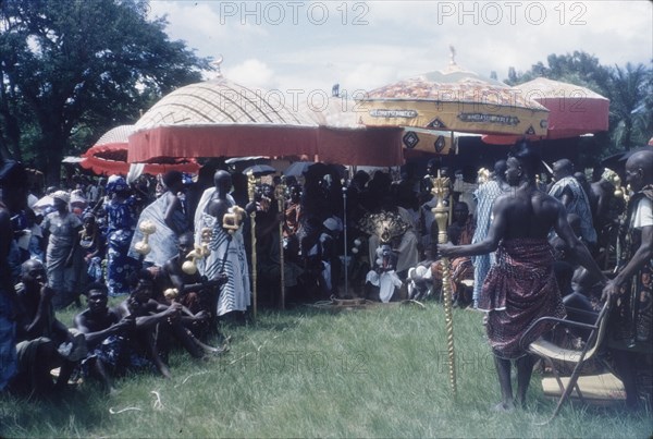 Mate Kole II at a Ngmayem festival. Mate Kole II (1910-1990), the Paramount Chief or Konor of Manya Krobo, sits beneath ceremonial umbrellas with his retinue at an annual Ngmayem harvest festival. He is attended by his 'okyeames' (linguists), each of whom carries a 'poma' (linguist's staff) as a badge of office. Odumasi, Ghana, circa 1960. Odumasi, East (Ghana), Ghana, Western Africa, Africa.