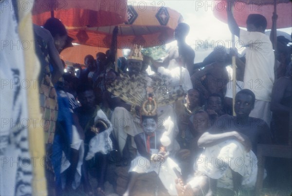 Mate Kole II at a Ngmayem festival. Mate Kole II (1910-1990), the Paramount Chief or Konor of Manya Krobo, sits beneath ceremonial umbrellas with his retinue at an annual Ngmayem harvest festival. The child with the painted face and elaborate headdress, seated at Mate Kole II's feet, represents the Konor's 'soul'. Odumasi, Ghana, circa 1960. Odumasi, East (Ghana), Ghana, Western Africa, Africa.