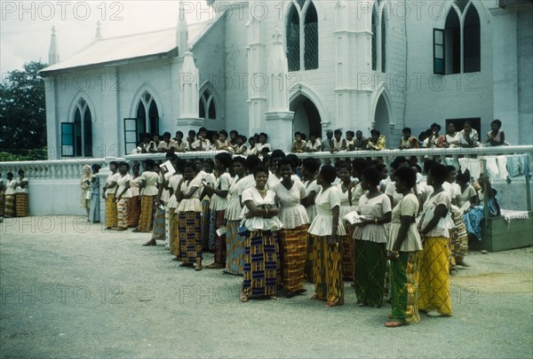 Students of a Wesleyan Girls' High School. Students of a Wesleyan Girls' High School gather outside a Methodist church at Cape Coast, dressed in a uniform of white blouses with skirts made from traditional kente cloth. Cape Coast, Ghana, 3 July 1960. Cape Coast, Central (Ghana), Ghana, Western Africa, Africa.
