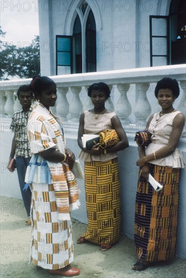 Students of a Wesleyan Girls' High School. Three students of a Wesleyan Girls' High School stand outside a Methodist church in Cape Coast, dressed in skirts made from traditional kente cloth. Cape Coast, Ghana, 3 July 1960. Cape Coast, Central (Ghana), Ghana, Western Africa, Africa.
