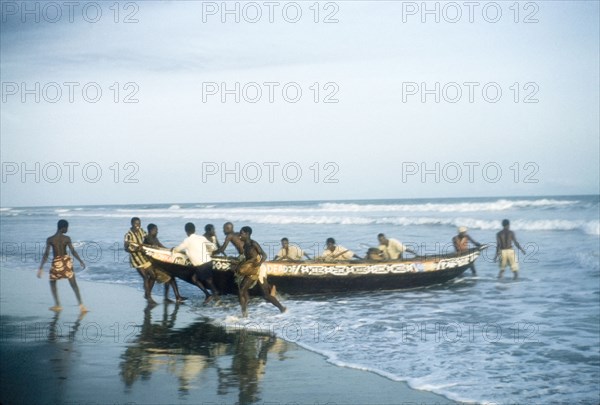 Beaching a boat in Saltpond. A group of men haul a painted fishing boat out of the sea and onto the beach. Saltpond, Ghana, circa 1960. Saltpond, West (Ghana), Ghana, Western Africa, Africa.