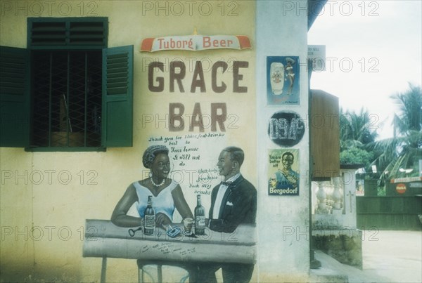 Advertisement for beer, Ghana. An advertisement painted on the exterior wall of a bar or shop features an African couple in Western-style clothing drinking bottles of beer and chatting. Saltpond, Ghana, 4 July 1960. Saltpond, West (Ghana), Ghana, Western Africa, Africa.