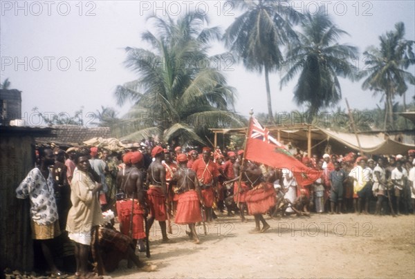 Flag dance of Asafo Number Two Company. A 'frankakitanyi' (flag dancer) swings the flag at the 'posuban' (military shrine) of Asafo Number Two Company in Lowtown. Saltpond, Ghana, April 1960. Saltpond, West (Ghana), Ghana, Western Africa, Africa.