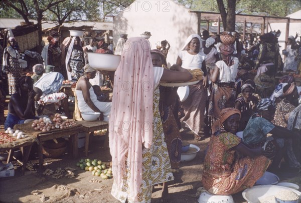 Dagomba woman at Tamale market. A woman wearing a traditional Dagomba veil carries containers of food through a bustling market. Tamale, Ghana, circa 1961. Tamale, North (Ghana), Ghana, Western Africa, Africa.