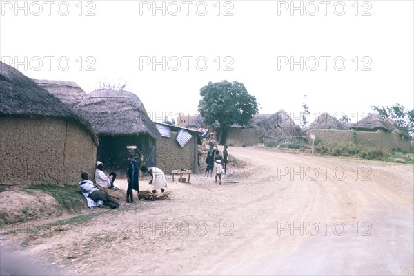 A Hausa village. View along a road running through a Hausa village, which is flanked by mud-walled, thatched buildings. Nigeria, October 1963. Nigeria, Western Africa, Africa.