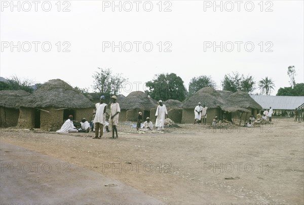 A Hausa village. Inhabitants of a Hausa village mill about outside several square, mud-walled huts with thatched roofs. Nigeria, October 1963. Nigeria, Western Africa, Africa.