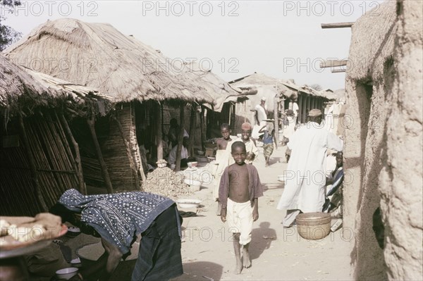 A marketplace in Kano. Thatched, open-fronted stalls line a busy marketplace in Kano. Kano, Nigeria, October 1963. Kano, Kano, Nigeria, Western Africa, Africa.