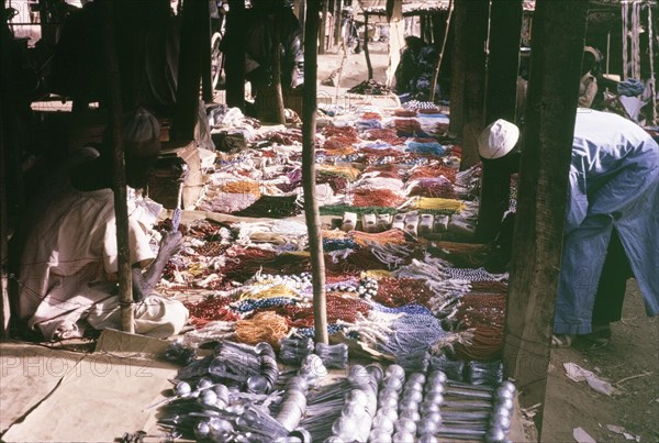 Beaded jewellery on a market stall. A customer bends down to inspect a huge selection of colourful beaded jewellery on a market stall. Kano, Nigeria, October 1963. Kano, Kano, Nigeria, Western Africa, Africa.