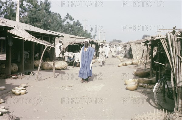 Marketplace in Kano. Stalls with thatched canopies shelter goods from the sun in a busy marketplace in Kano. Kano, Nigeria, 1963. Kano, Kano, Nigeria, Western Africa, Africa.