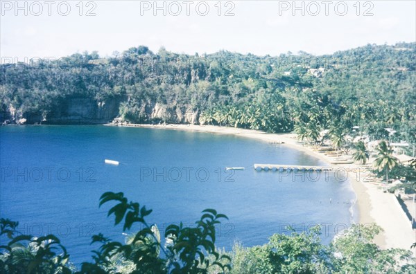 A fishing bay in St Lucia. View over a bay at St Lucia, where fishing boats are moored on the beach and a pier stretches out into the Caribbean Sea. St Lucia, circa 1975. St Lucia, Caribbean, North America .