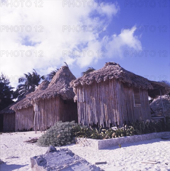 Beach huts at San Pedro, Belize. Four square, bamboo beach huts with thatched roofs stand in a row on the beachfront at San Pedro. Ambergris Caye, Belize, circa 1975. San Pedro, Ambergris Caye, Belize, Central America, North America .