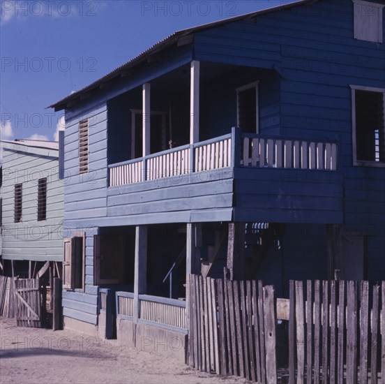 A blue house in Belize. Exterior view of a wooden, two-storey house in Belize. The building has been painted blue and features a balcony and veranda. Belize, circa 1975. Belize, Central America, North America .