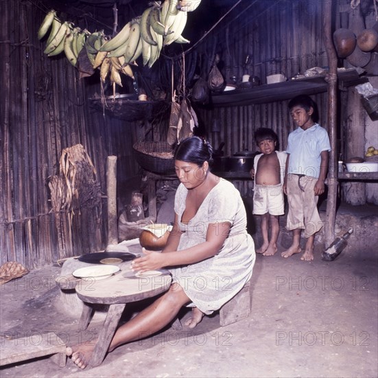 Preparing tortillas, Belize. A Ketchi woman sits at a low table indoors, preparing tortillas under the watchful eye of two young boys. Belize, circa 1975. Belize, Central America, North America .