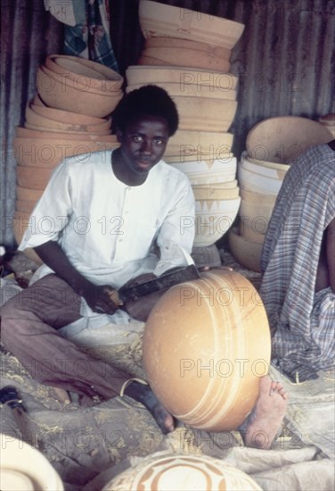 A Hausa potter decorates a bowl. A Hausa potter uses a metal tool to inscribe patterns onto a clay bowl. Kano, Nigeria, circa 1975. Nigeria, Western Africa, Africa.