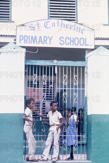 Children at St Catherine's Primary School. An official publicity shot for the Jamaican Tourist Board features four schoolchildren chatting beside an iron gate outside St Catherine's Primary School. Spanish Town, Jamaica, circa 1985. Spanish Town, St Catherine, Jamaica, Caribbean, North America .