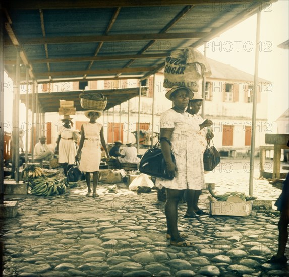 Dominican women at a street market. Dominican women at a street market carry their shopping in sacks, baskets and crates balanced on their heads. Dominica, circa 1975. Dominica, Caribbean, North America .
