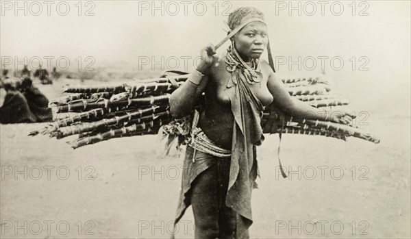 Kikuyu woman carrying canes. A Kikuyu woman carries a bundle of canes on her back, supported by a strap across her forehead. British East Africa (Kenya), circa 1912. Kenya, Eastern Africa, Africa.