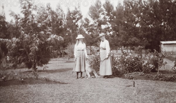Mrs Elkington poses with her pet lion. Mrs Elkington and her daughter, Margaret, pose in their garden with their pet lion cub, Paddy. British East Africa (Kenya), circa 1910. Kenya, Eastern Africa, Africa.
